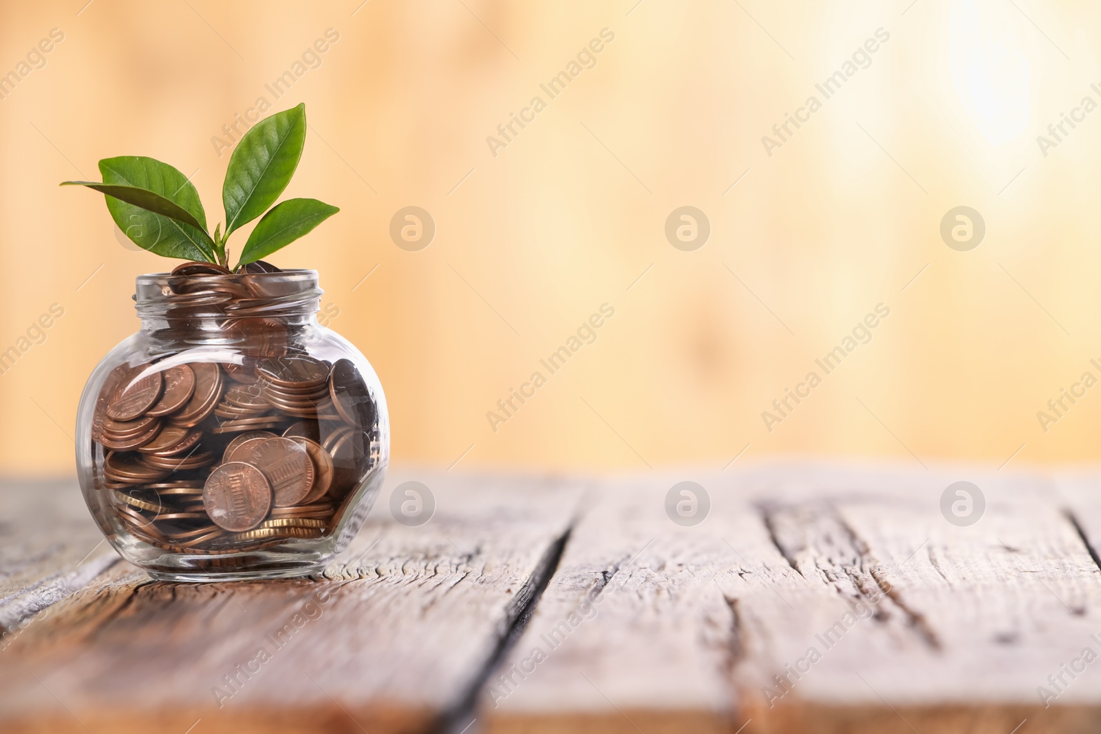 Investment concept. Glass jar with coins and sprout on wooden table against blurred orange background, space for text Photo of Investment concept. Glass jar with coins and sprout on wooden table against blurred orange background, space for text