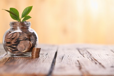 Photo of Investment concept. Glass jar with coins and sprout on wooden table against blurred orange background, space for text
