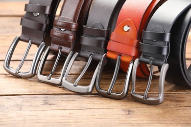 Photo of Many different leather belts on wooden table, closeup