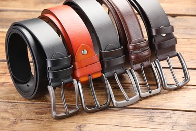 Photo of Many different leather belts on wooden table, closeup