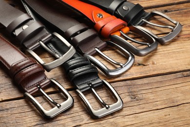 Photo of Many different leather belts on wooden table, closeup