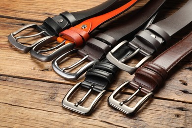 Photo of Many different leather belts on wooden table, closeup