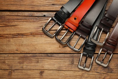 Photo of Many different leather belts on wooden table, flat lay. Space for text