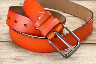 Photo of One orange leather belt on wooden table, closeup