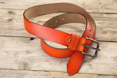 Photo of One orange leather belt on wooden table, above view