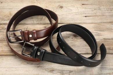 Photo of Two leather belts on wooden table, above view