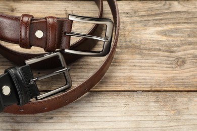 Photo of Two leather belts on wooden table, above view. Space for text