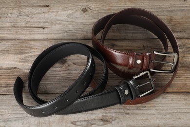 Photo of Two leather belts on wooden table, above view
