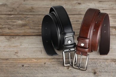 Photo of Two leather belts on wooden table, closeup. Space for text
