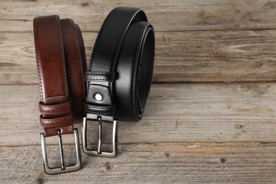 Photo of Two leather belts on wooden table, closeup. Space for text
