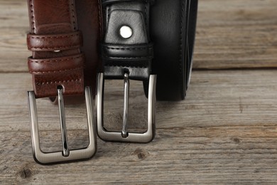 Photo of Two leather belts on wooden table, closeup. Space for text