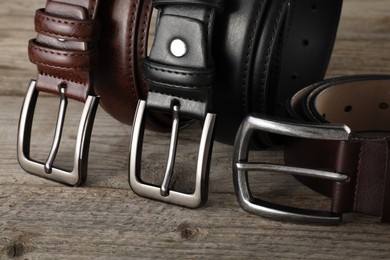 Photo of Three leather belts on wooden table, closeup
