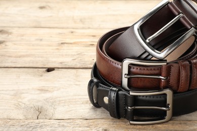 Photo of Three leather belts on wooden table, closeup. Space for text