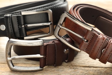 Photo of Three leather belts on wooden table, closeup