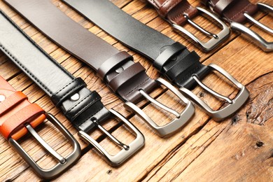 Photo of Many different leather belts on wooden table, above view
