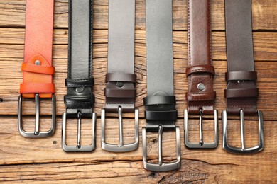 Photo of Many different leather belts on wooden table, flat lay