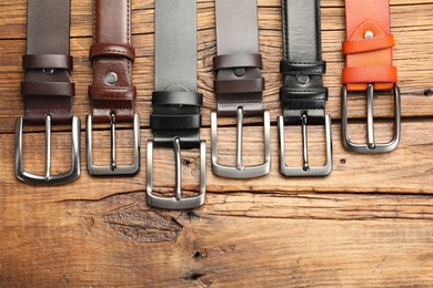Photo of Many different leather belts on wooden table, flat lay