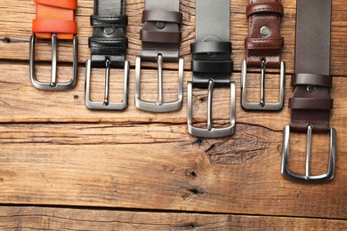 Photo of Many different leather belts on wooden table, flat lay. Space for text