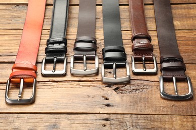 Photo of Many different leather belts on wooden table, above view