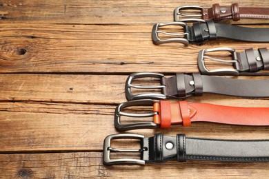 Photo of Many different leather belts on wooden table, above view. Space for text