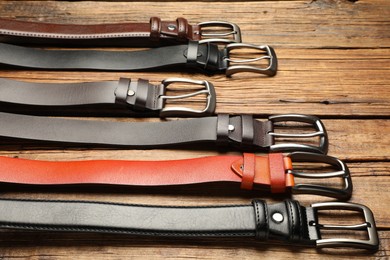 Photo of Many different leather belts on wooden table, closeup