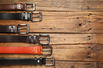 Photo of Many different leather belts on wooden table, flat lay. Space for text