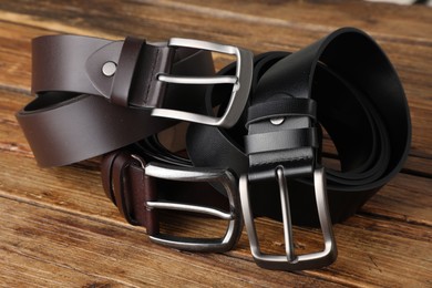 Photo of Three leather belts on wooden table, closeup