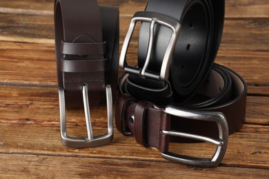 Photo of Three leather belts on wooden table, closeup