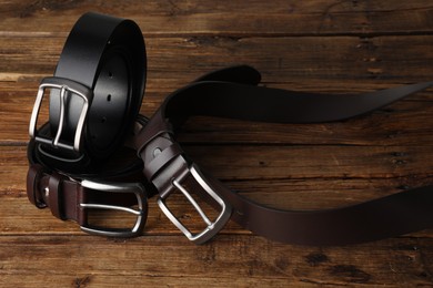 Photo of Three leather belts on wooden table, closeup