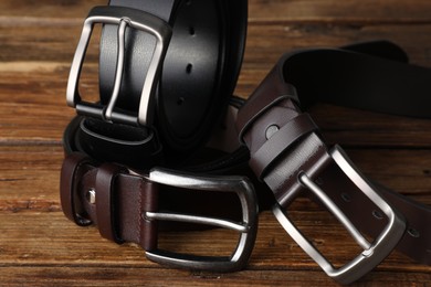 Photo of Three leather belts on wooden table, closeup