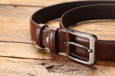 Photo of One brown leather belt on wooden table, closeup. Space for text