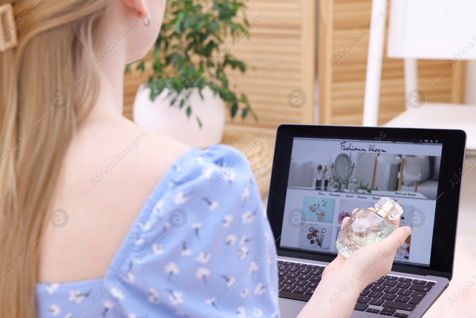Photo of Blogger holding perfume near laptop with fashion blog web site indoors, closeup