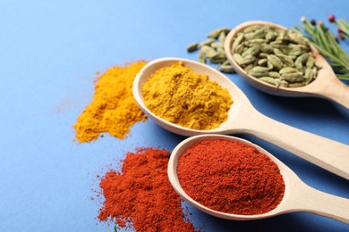 Photo of Different aromatic spices in spoons on blue background, closeup