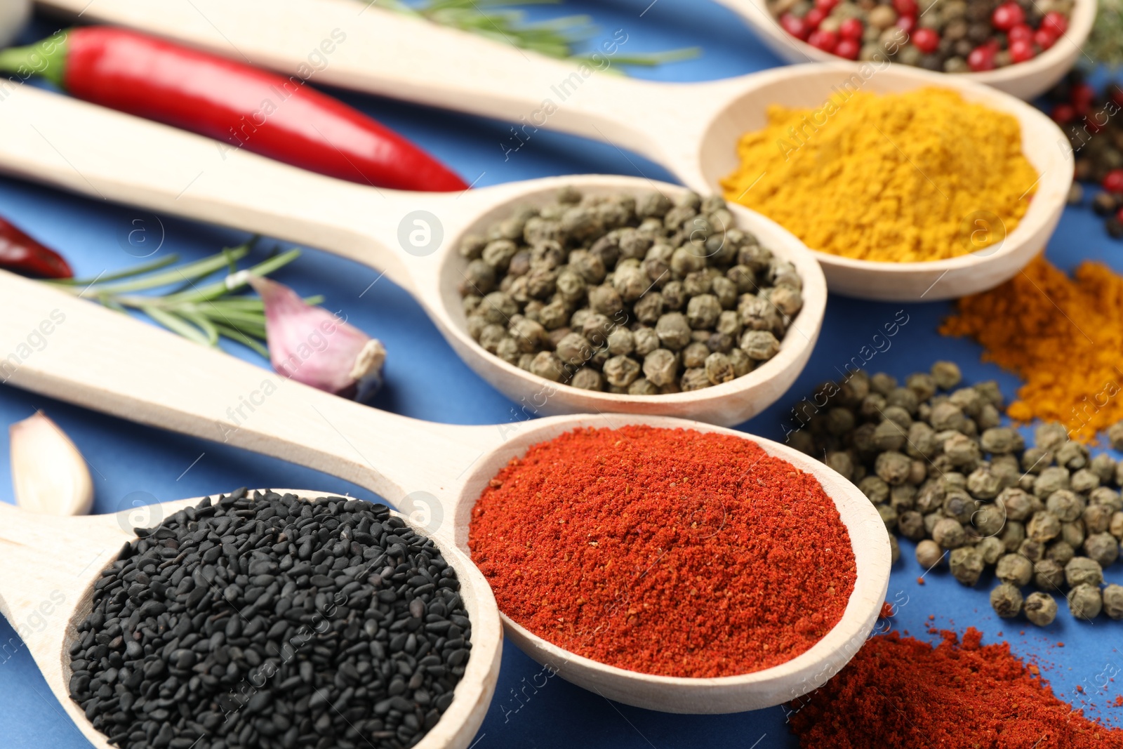 Different aromatic spices in spoons on blue background, closeup Photo of Different aromatic spices in spoons on blue background, closeup