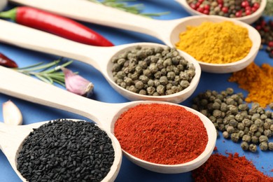 Photo of Different aromatic spices in spoons on blue background, closeup
