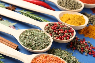 Photo of Different aromatic spices in spoons on blue background, closeup
