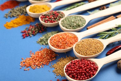 Photo of Different aromatic spices in spoons on blue background, closeup
