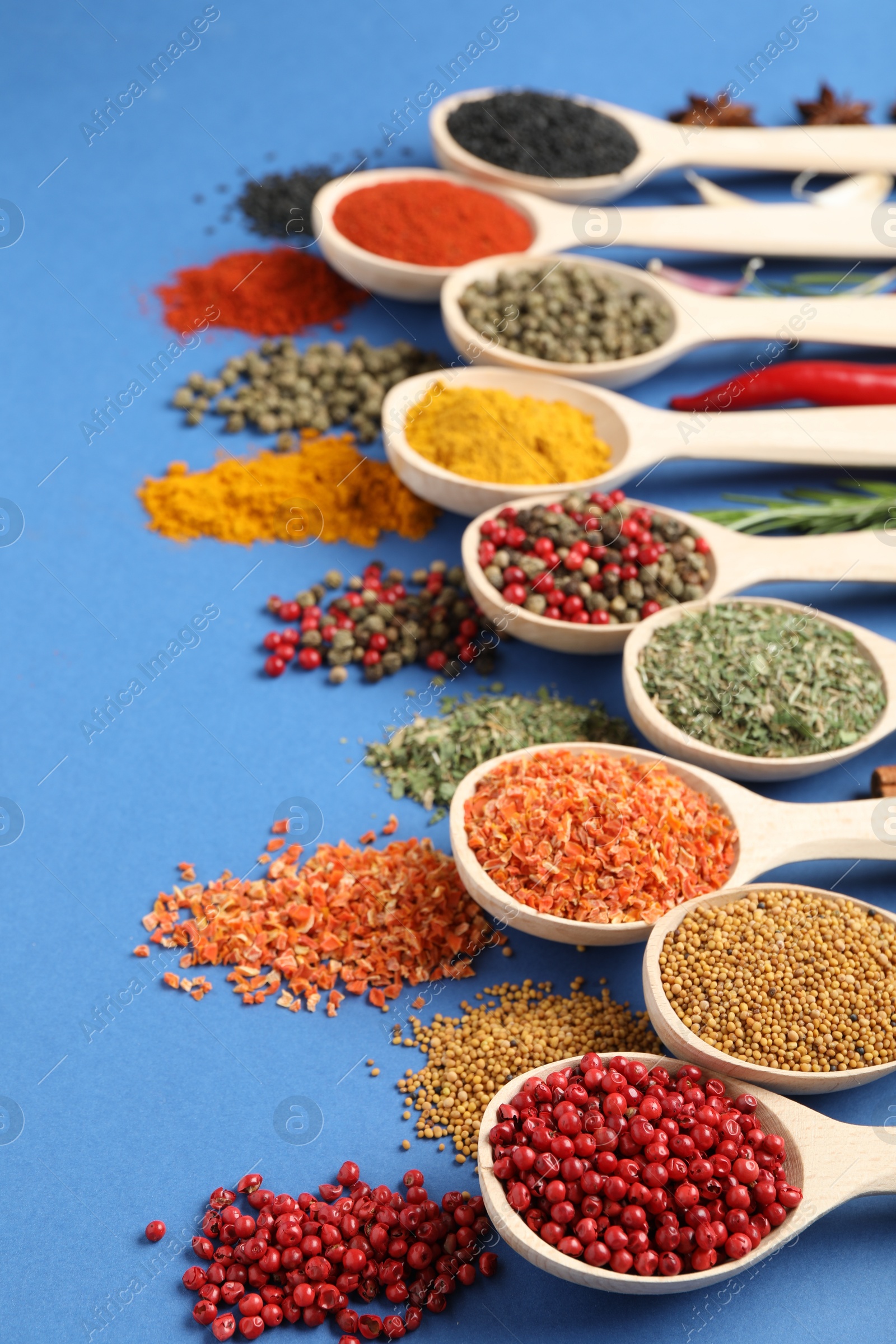 Different aromatic spices in spoons on blue background, closeup Photo of Different aromatic spices in spoons on blue background, closeup