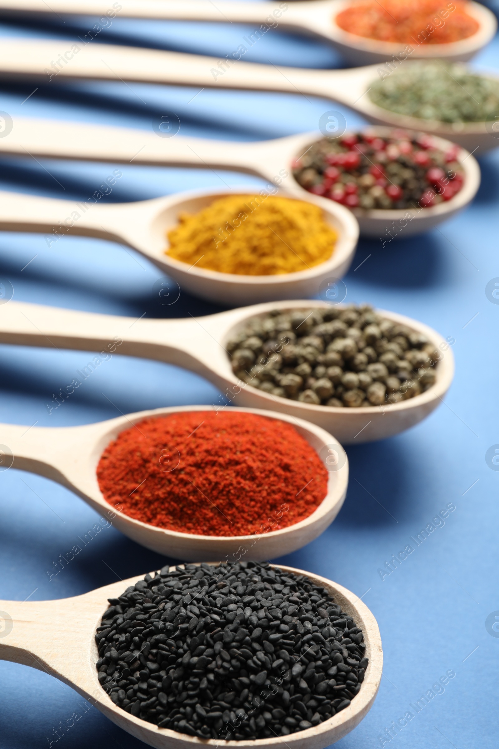 Different aromatic spices in spoons on blue background, closeup Photo of Different aromatic spices in spoons on blue background, closeup