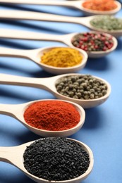 Photo of Different aromatic spices in spoons on blue background, closeup