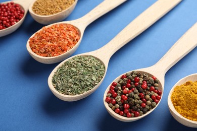 Photo of Different aromatic spices in spoons on blue background, closeup