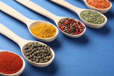 Photo of Different aromatic spices in spoons on blue background, closeup