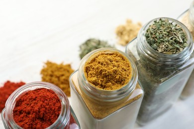 Photo of Different aromatic spices in jars on white table, closeup
