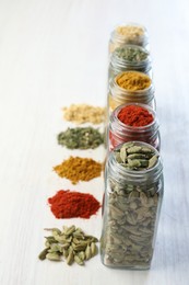 Photo of Different aromatic spices in jars on white table, closeup