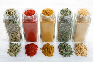 Photo of Different aromatic spices in jars on white table, closeup