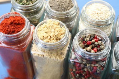 Photo of Different aromatic spices in jars on blue background, closeup