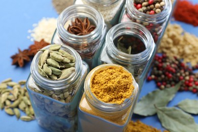 Photo of Different aromatic spices in jars on blue background, closeup