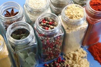 Photo of Different aromatic spices in jars on blue background, closeup