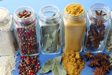 Photo of Different aromatic spices in jars on blue background, closeup