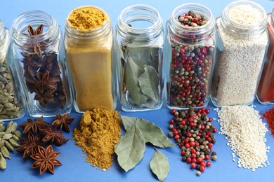 Photo of Different aromatic spices in jars on blue background, closeup